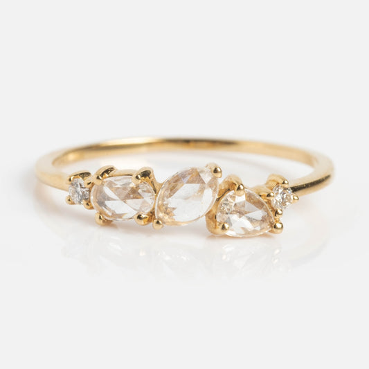 The Cosmos Ring, crafted in 14k yellow gold, features three pear-shaped clear gemstones set side by side and a small round diamond on each end, displayed against a white background.