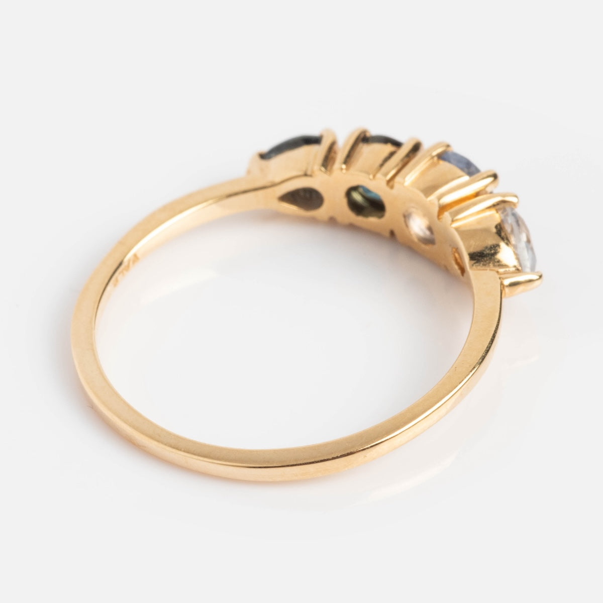 The Harmony Ring is a 14k gold piece with a slim band, showcasing multiple blue sapphires set in a row along the top, seen from an angle that reveals the elegant side and underside of its settings.