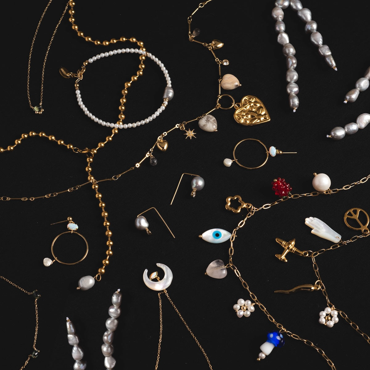 The Goals Charm Necklace features gold and pearl charms shaped like hearts, moons, flowers, eyes, and shells—all beautifully displayed on a black background.