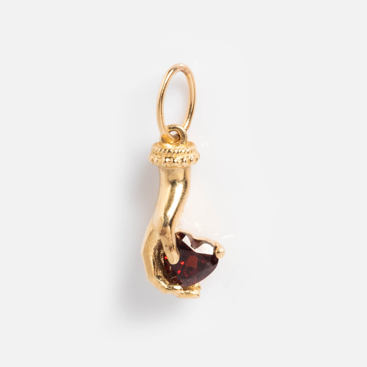 The Solid Gold Body Language Charm, a Local Eclectic exclusive, features a hand holding a red heart-shaped gemstone and a small loop for attaching to jewelry, shown on a plain white background.