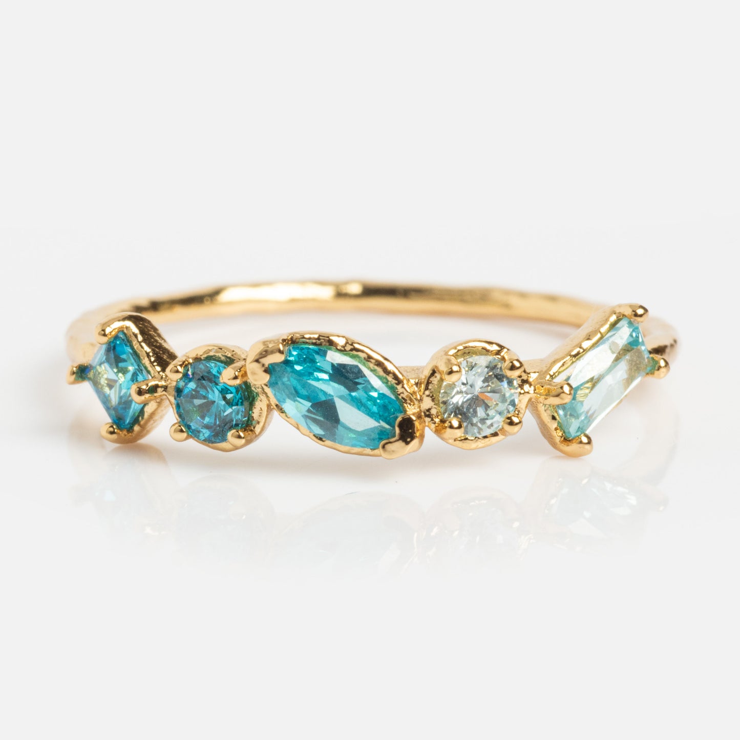 The Shades of You Ombre Birthstone Ring features five blue gemstones in round, oval, and marquise cuts set in a row on a 14k gold plated band—an elegant birthstone jewelry piece displayed on a white background.