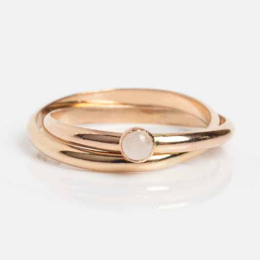 The Gold Orbit Meditation Ring is a 14k yellow gold filled ring with two interlocking bands, one featuring a small round moonstone in a simple bezel, shown on a white surface.