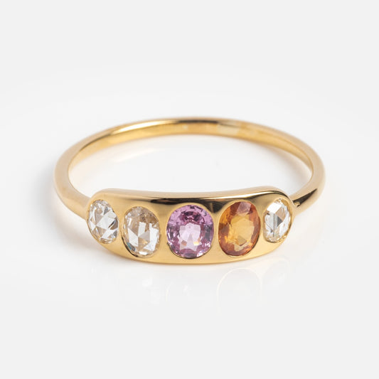 The Asha Ring with Mixed Sapphire in 14k yellow gold showcases five sapphires—two clear, one pink, one orange, and another clear—set in a row on a simple gold band.