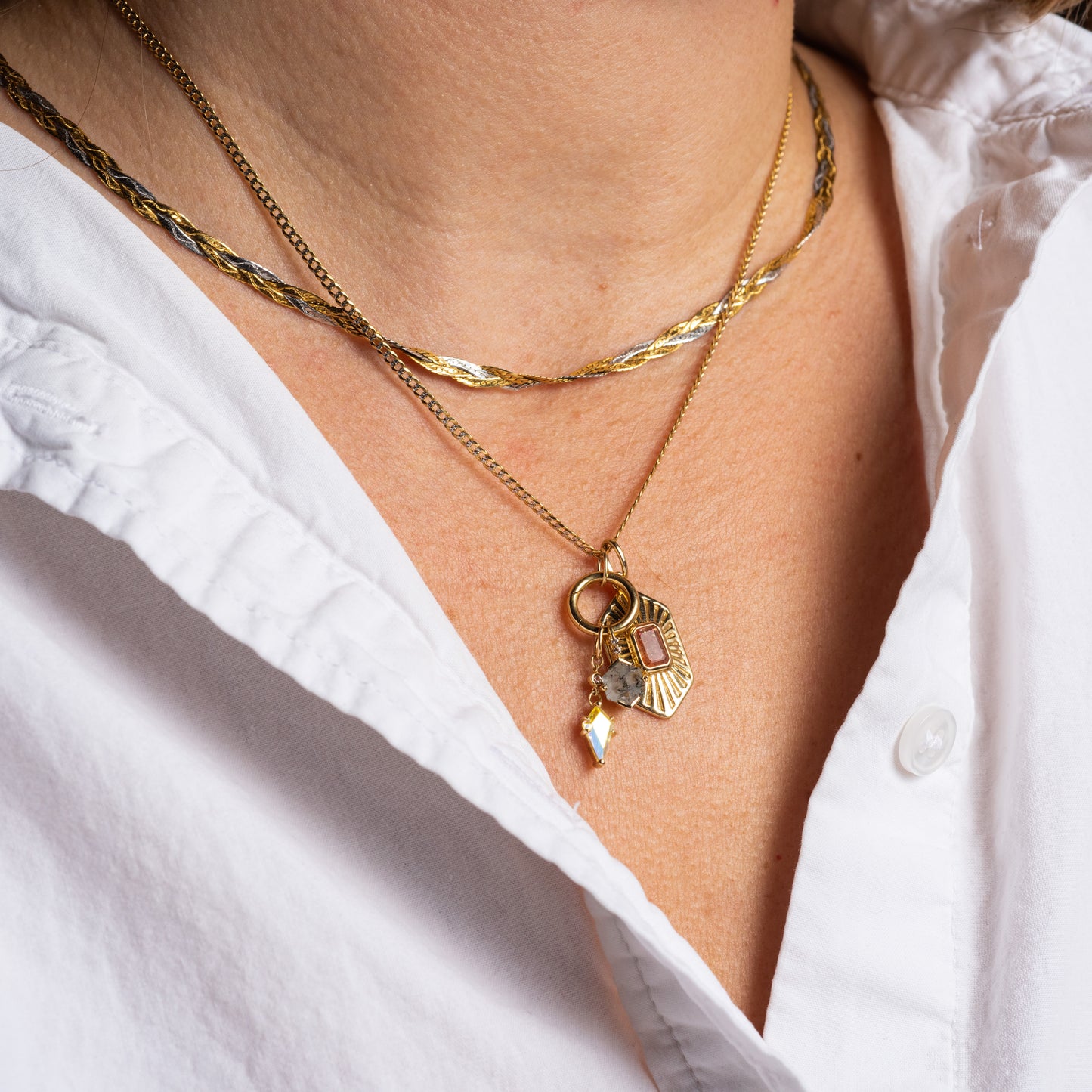 Close-up of a person in a white collared shirt wearing two gold necklaces: one plain, the other adorned with gemstone accents and three pendants, including a rectangular gem and the Solid Gold Amulet Charm.