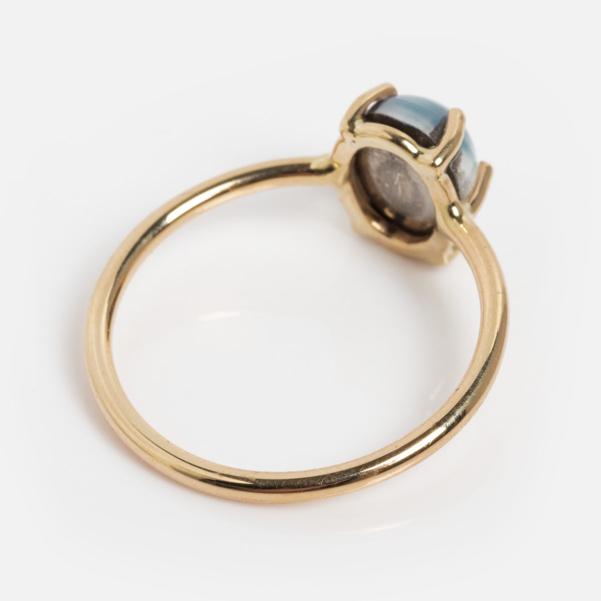 The 14k Blue Crush Cats Eye Moonstone Solitaire Ring features a delicate round blue cats eye moonstone in a prong setting, shown from the side on a white background.