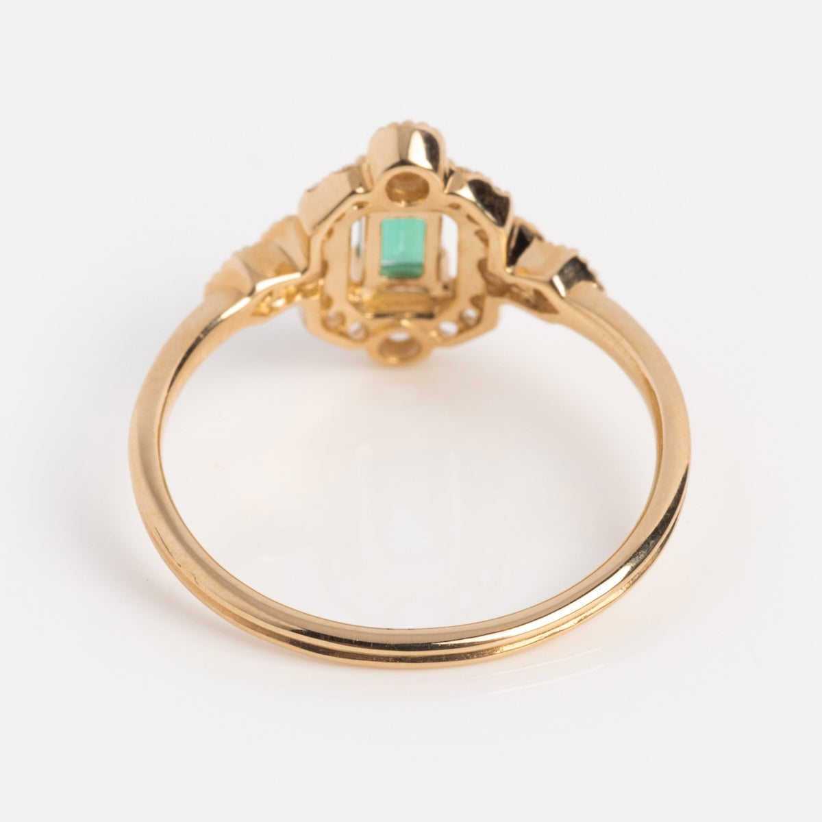 The 14k Vintage Inspired Emerald Shield Ring features a rectangular green gemstone in an ornate setting, centered on a 14k gold band and shown from the back against a plain white background.