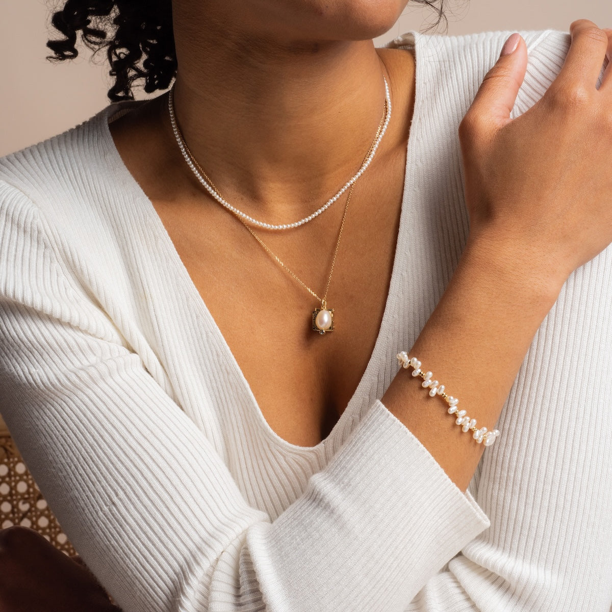 A woman in a white ribbed top displays elegant jewelry—a double-layered pearl and blue topaz pendant necklace, a pearl bracelet, and the Solid Gold Statement Charm—as her hand rests near her collarbone in a relaxed pose.