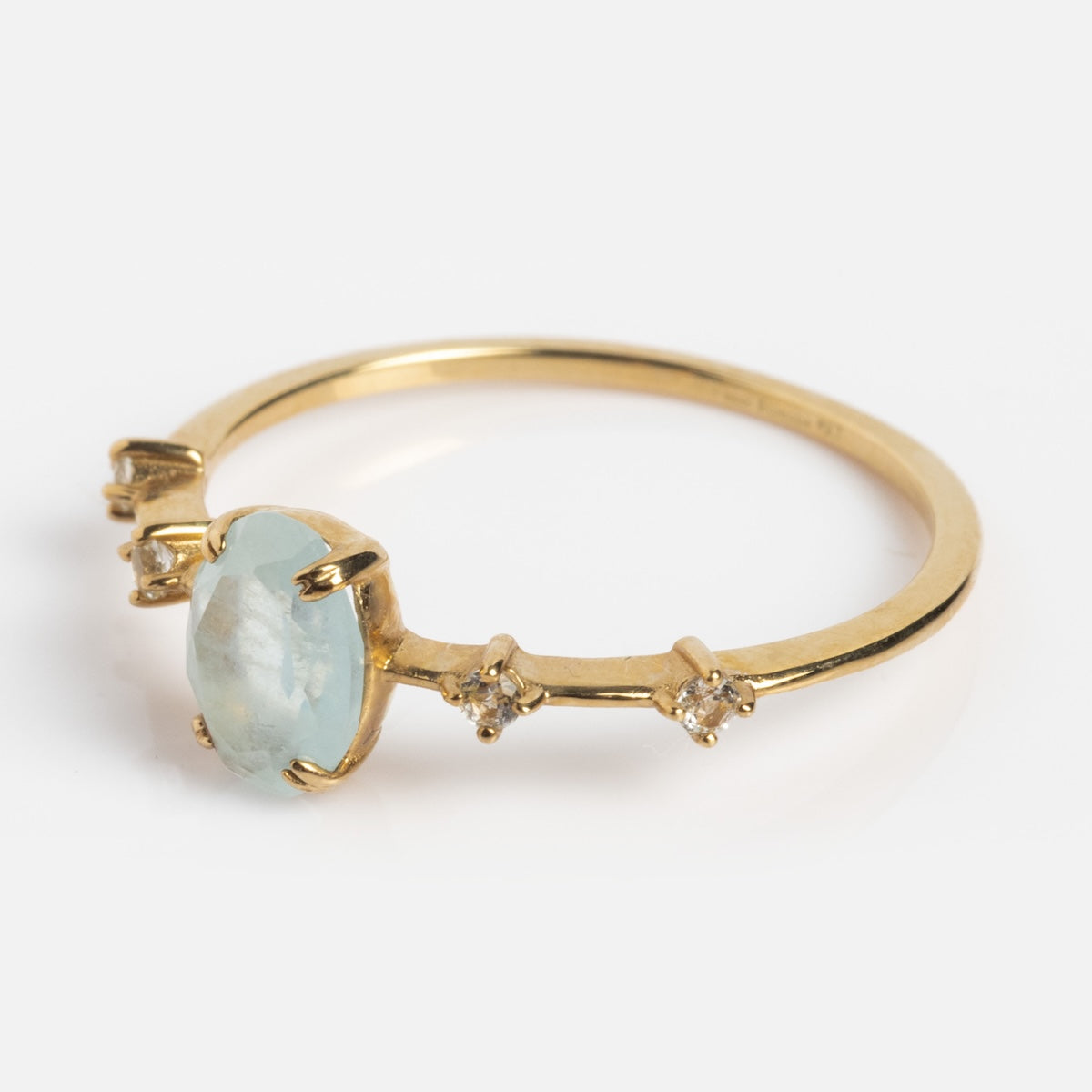 The Solid Gold 2025 March Capsule Classic Aquamarine Statement Ring features an oval pale blue center stone and three round clear accents on each side, displayed on a white background—an elegant birthstone ring for March.