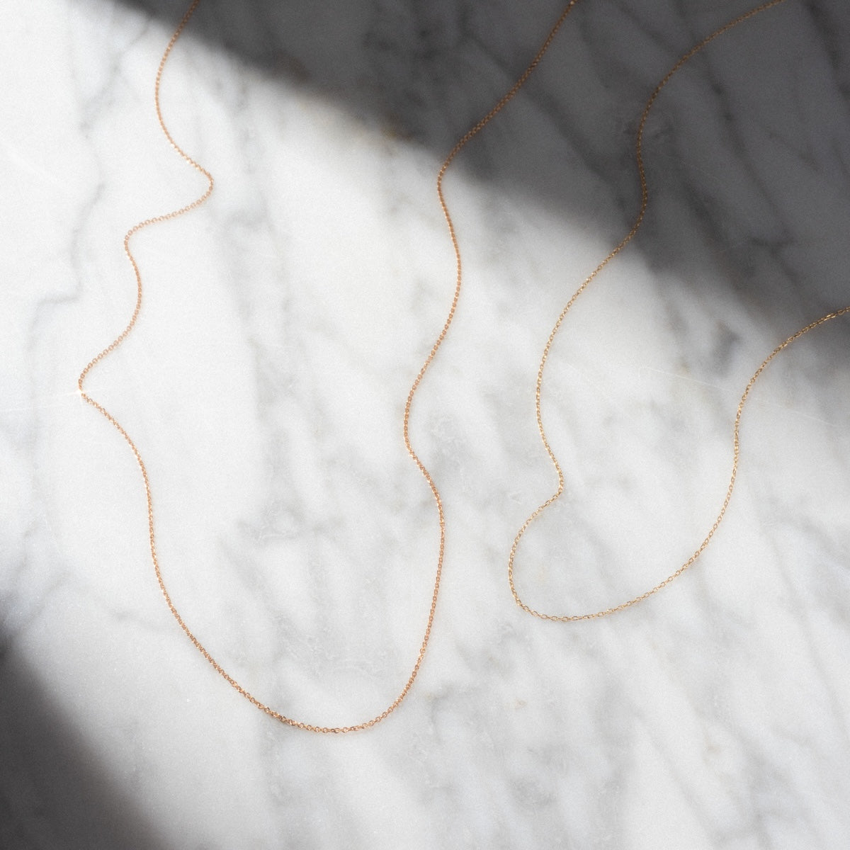 The Solid Gold Chain for Charms is displayed in gentle curves on a white marble surface, with soft shadows adding elegance to the scene.