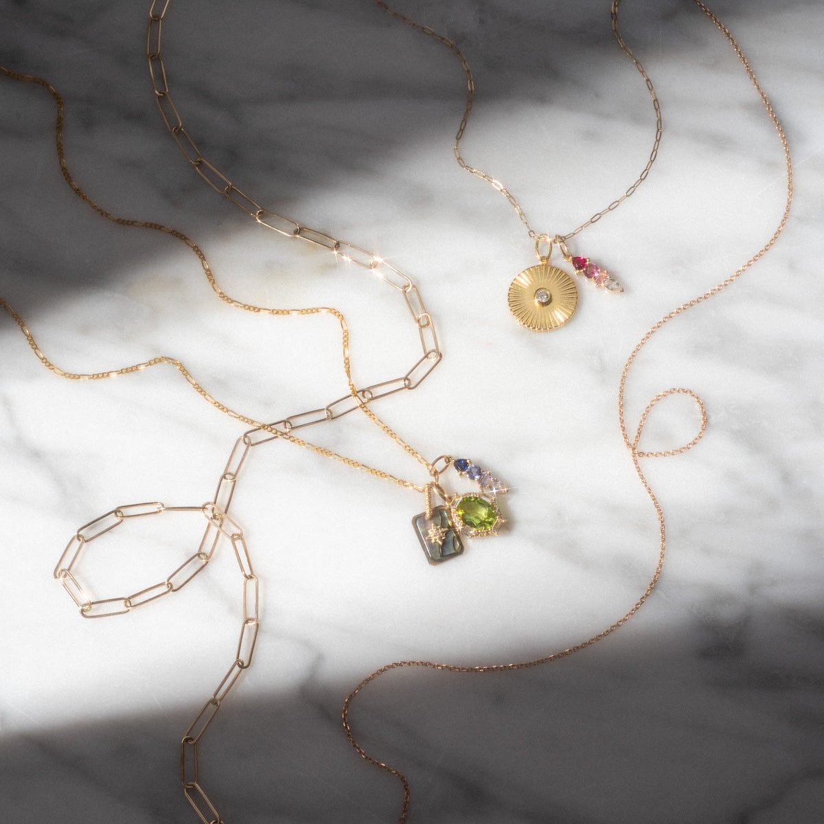 The Solid Gold Chain for Charms is displayed with two other gold necklaces on a marble surface, as sunlight casts gentle shadows over the arrangement.