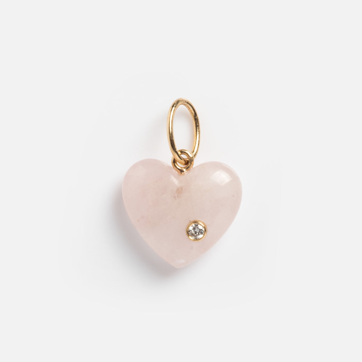 The Solid Gold Full Heart Crystal Charm is a heart-shaped pale pink pendant with a small gold loop and a single sparkling gem set at the lower right, shown against a white background.