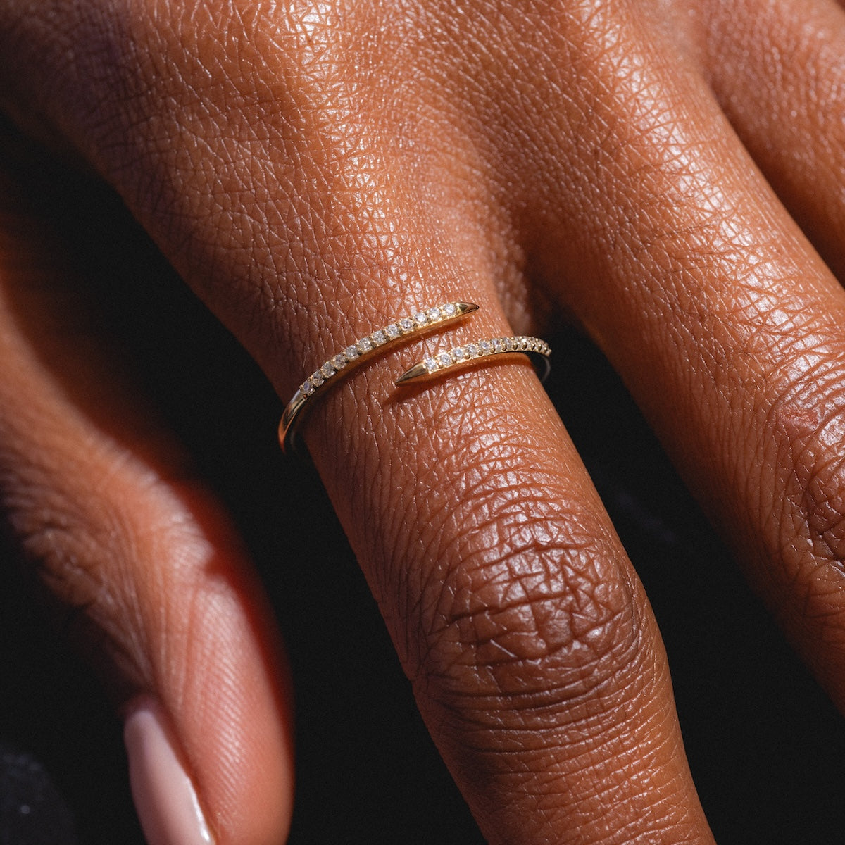 A close-up of a hand wearing the Solid Gold 2025 April Capsule White Topaz Wrapped Stacking Ring, elegantly wrapped around the finger against a dark background.