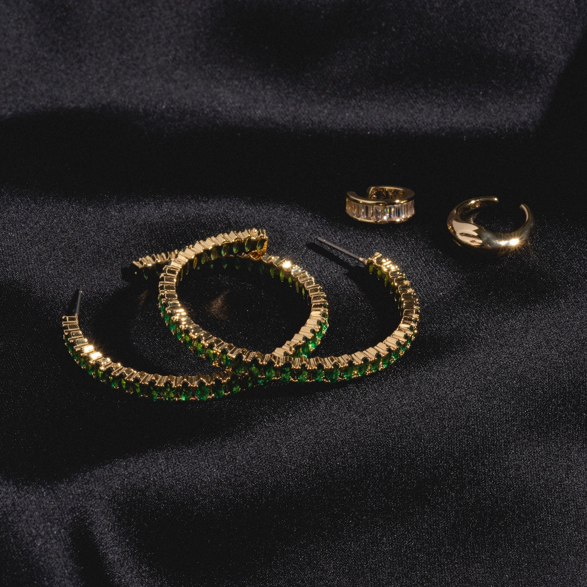 Emerald Marquise Hoops are displayed elegantly on a black satin fabric background.