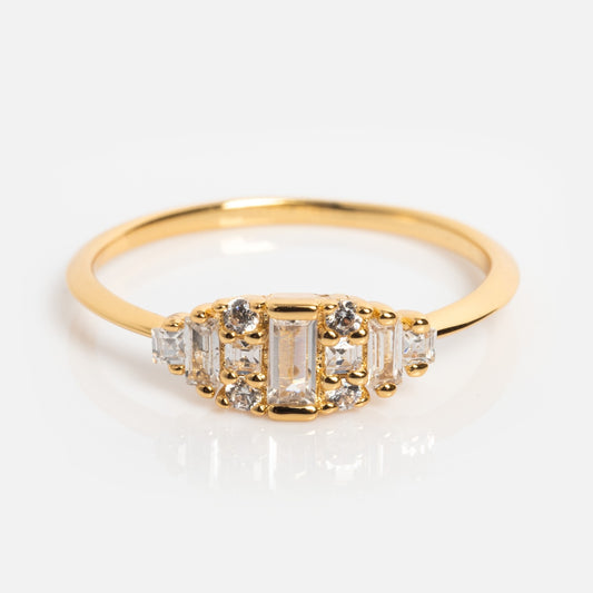 The Soiree Vintage Inspired Ring features a central rectangular white CZ, accented by round and baguette stones in a symmetrical design on a 14k gold plated band, displayed on a light background.