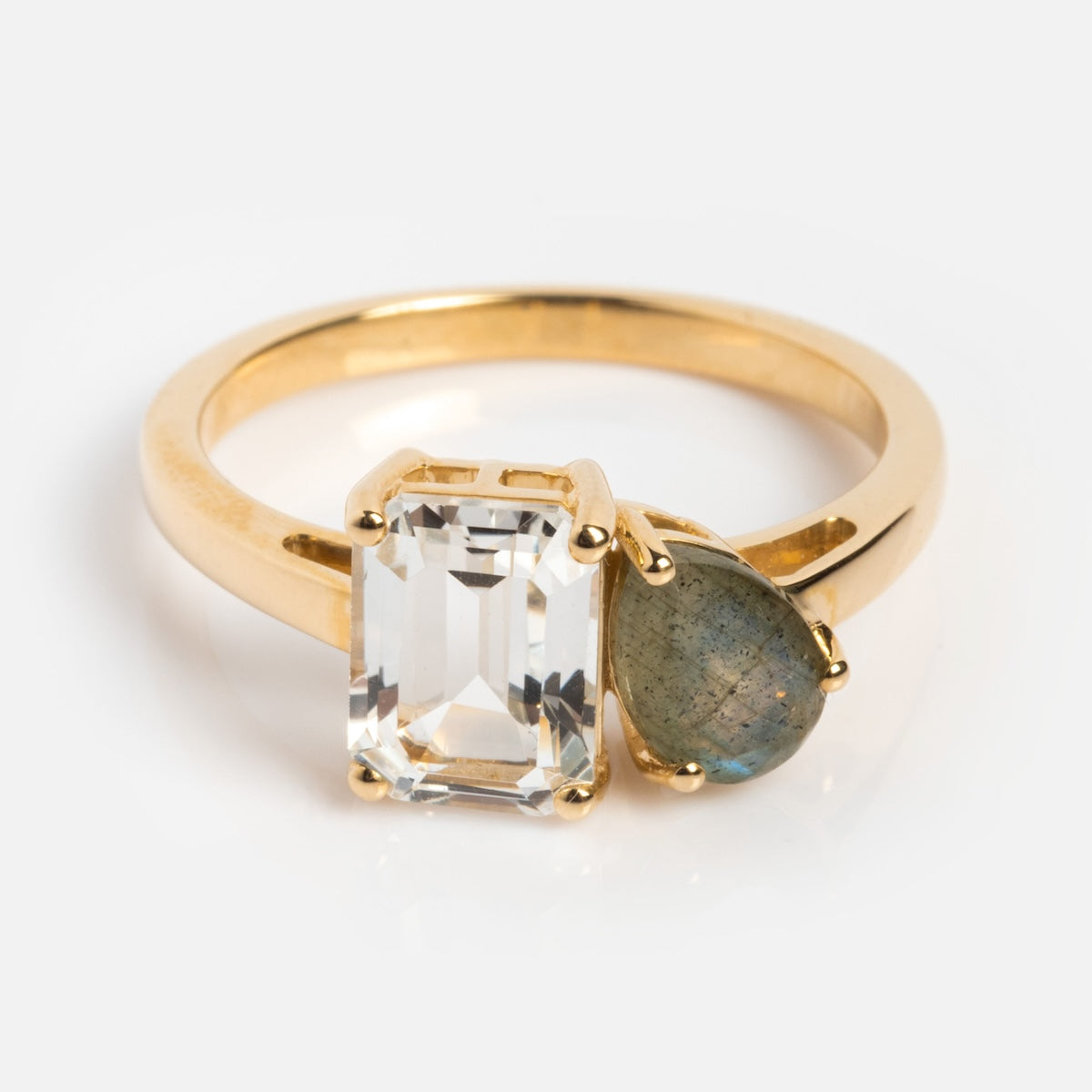 The Customizable Toi et Moi Ring in solid gold features a rectangular clear gemstone alongside a teardrop grayish-green stone, shown against a white background.