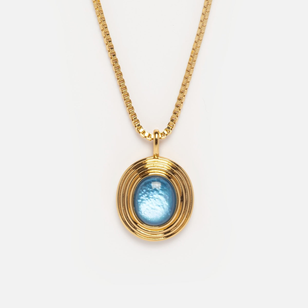 The Saturn Blue Mother of Pearl Pendant Necklace Sample features a 14k yellow gold plated thin box chain and an oval blue gemstone pendant with concentric gold rings, shown against a plain white background.