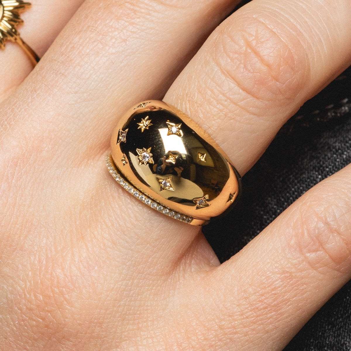 A close-up of a hand wearing the Cosmic Dome XL Ring Sample Size 8—shiny 14k yellow gold plating with star engravings and CZ diamonds—on the middle finger, with other gold rings on adjacent fingers.