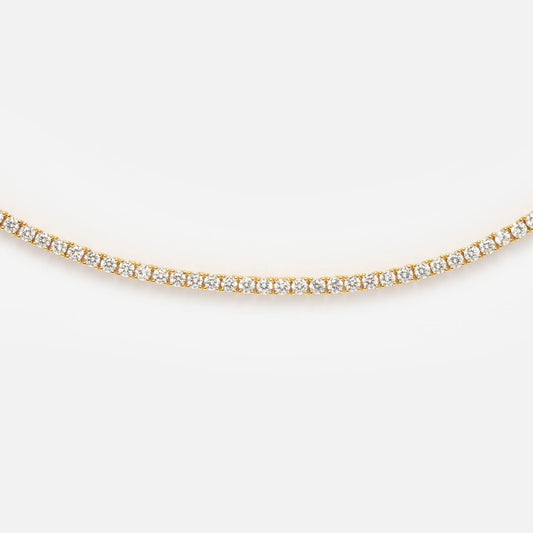 A close-up of the Tennis Necklace, showcasing a continuous row of small, round white diamonds set closely together in 14k yellow gold plating against a white background.