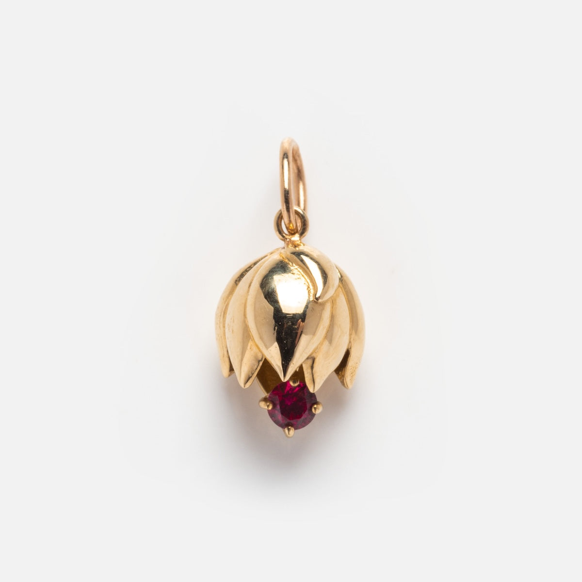 The Solid Gold Birth Flower Bud Charm features overlapping gold petals encircling a red gemstone at the center, suspended from a circular gold loop and displayed against a plain white background.