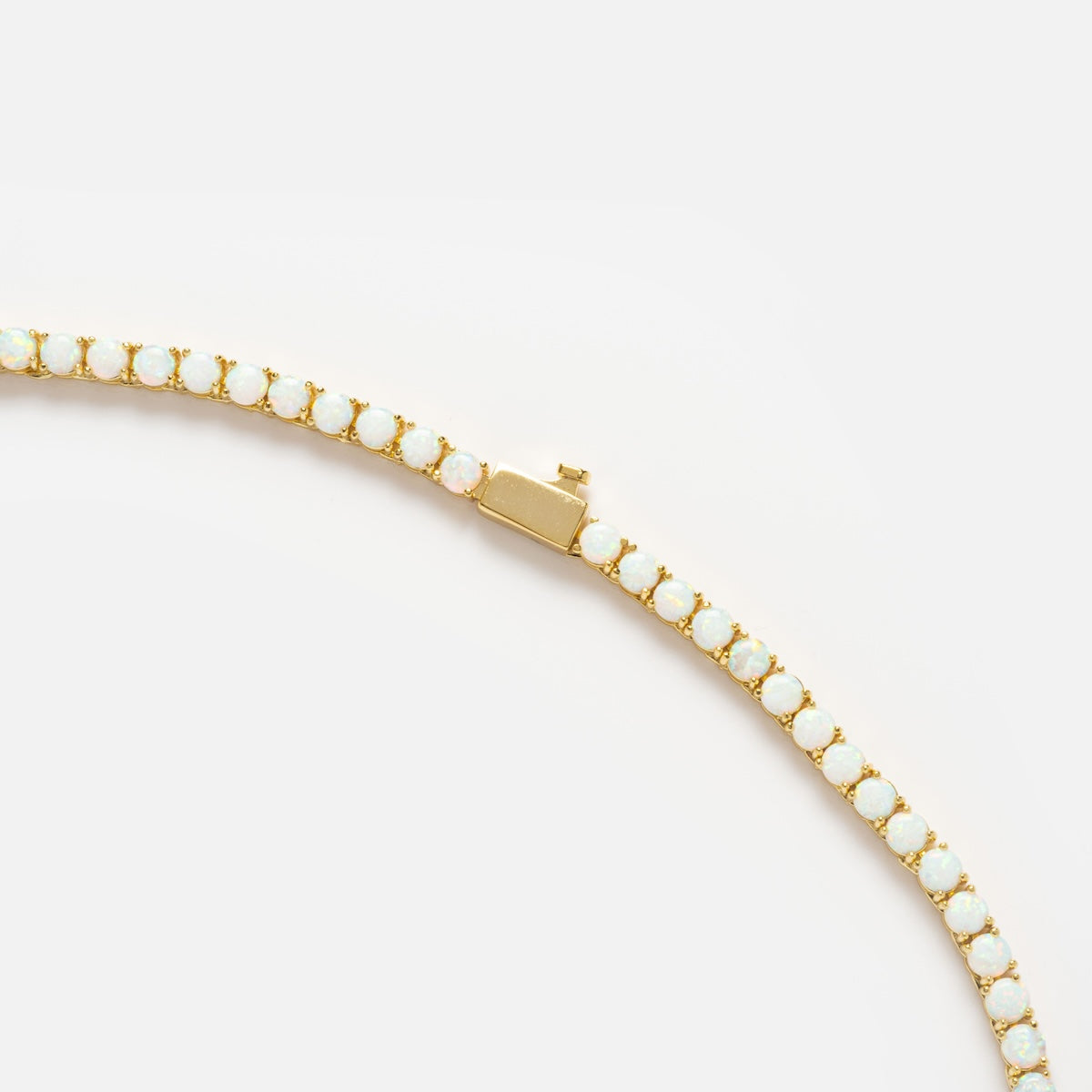 A close-up of the Grand Heiress Tennis Necklace, an 18k gold plated piece featuring a row of round white opal gemstones in gold prongs, displayed on a white background.
