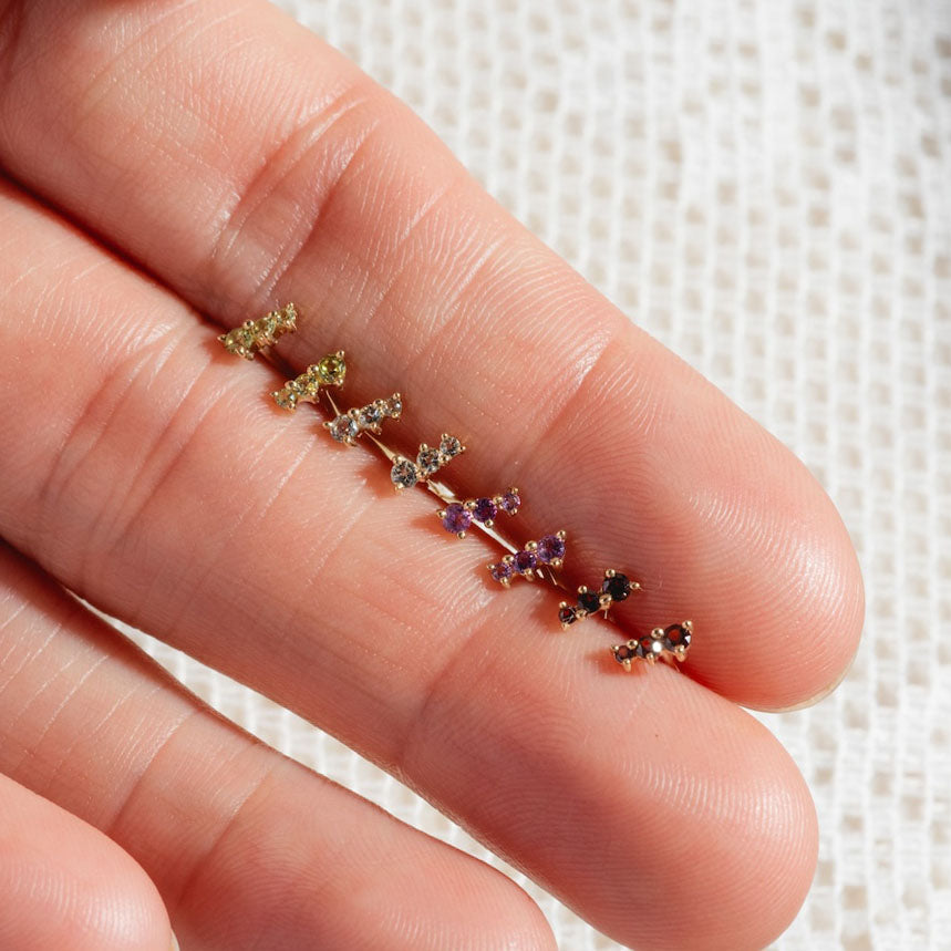 A close-up of a hand holding Solid Gold Dainty Birthstone Bar Studs, each earring featuring personalized colorful gemstones and elegantly arranged by size on the fingers.