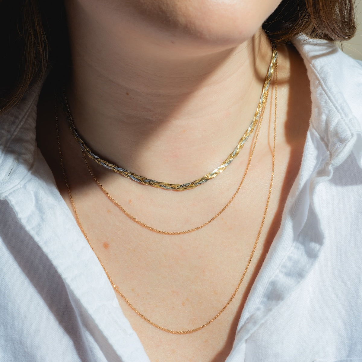 A person wearing a white shirt and three layered necklaces: the Solid Gold Simple Glimmer Gold Chain, plus two thin, delicate 9k gold necklaces draped elegantly around their neck.