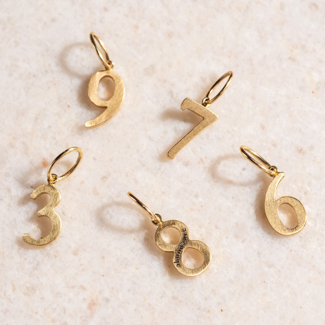 Five Solid Gold Number Charms—3, 6, 7, 8, and 9—are displayed on a light textured surface. Each Solid Gold Number Charm has a small loop for attaching to chains or bracelets, ideal for making personalized jewelry.