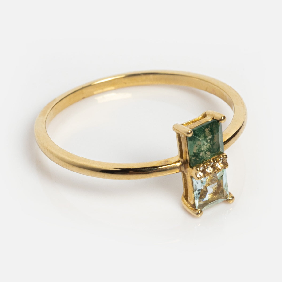 The Solid Gold Toi et Moi North South Ring showcases a slim gold band with a rectangular green gemstone and a smaller clear stone set vertically side by side, each secured by delicate gold prongs.