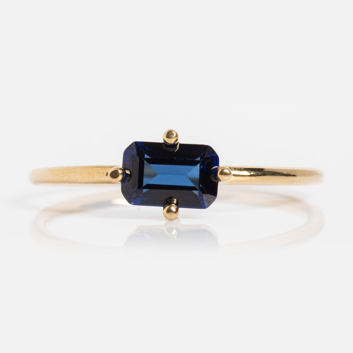 The 14k Mod Love Birthstone Ring features an emerald-cut deep blue gemstone in a four-prong yellow gold setting, shown against a white background.