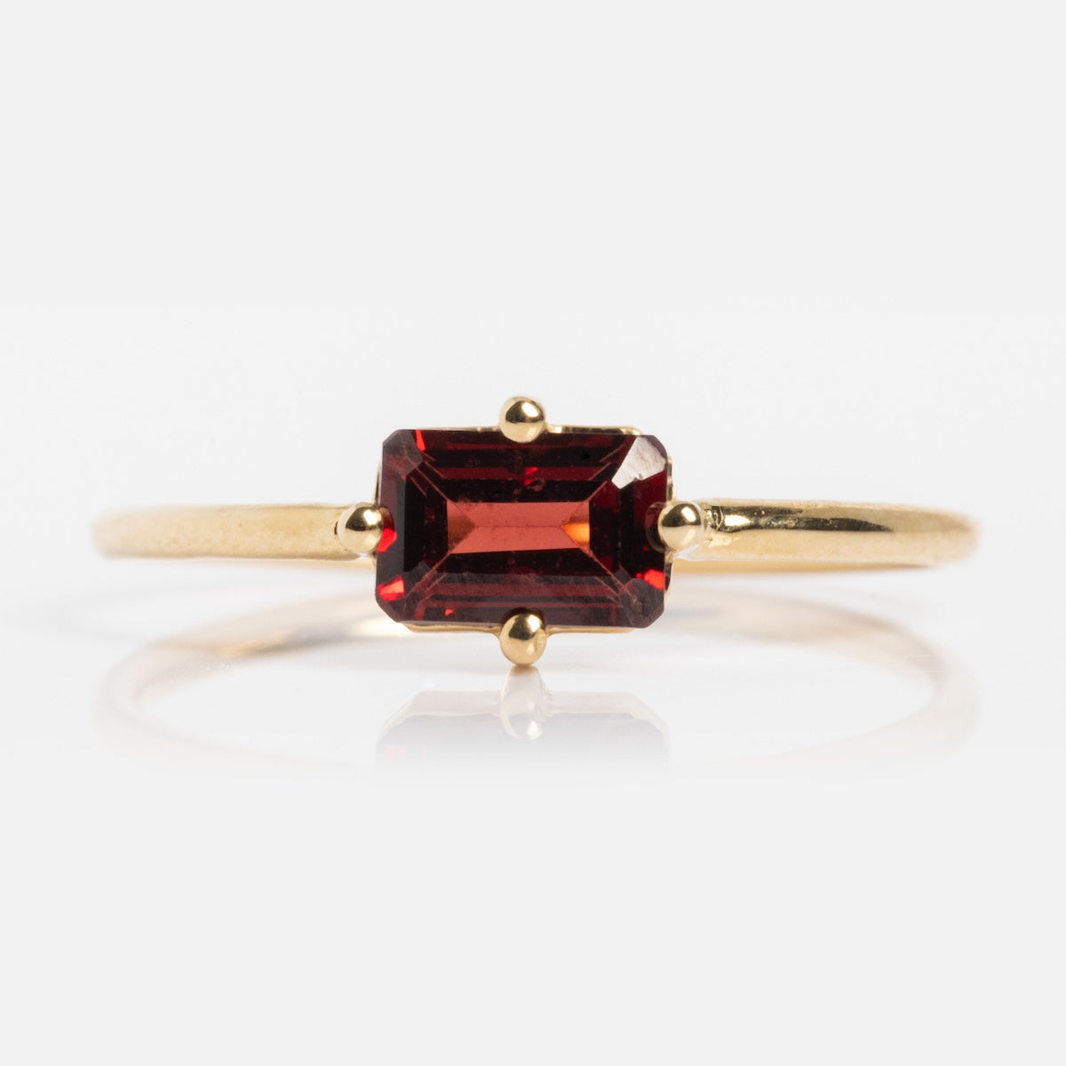 The 14k Mod Love Birthstone Ring showcases a rectangular, emerald-cut deep red gemstone set in a four-prong setting on a sleek, polished gold band.