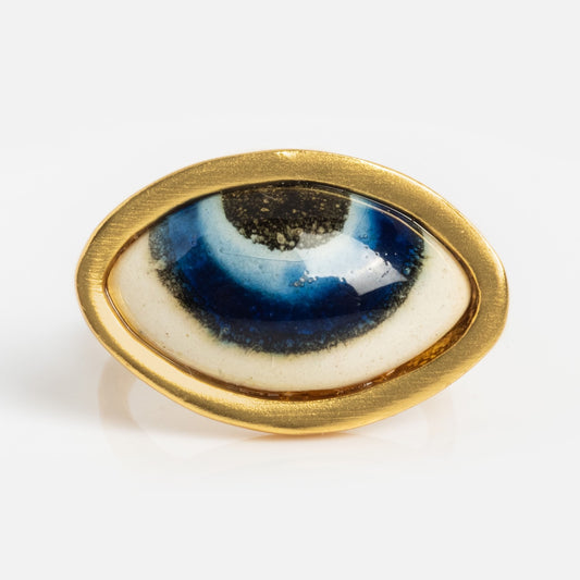 The Adira Blue Porcelain Evil Eye Ring features a stylized blue and black eye design with a glossy finish, set against a white backdrop.