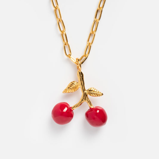 The Juicy Cherry Necklace features a gold-plated chain with a bold pendant of two red cherries and gold leaves, adding playful charm to any outfit.