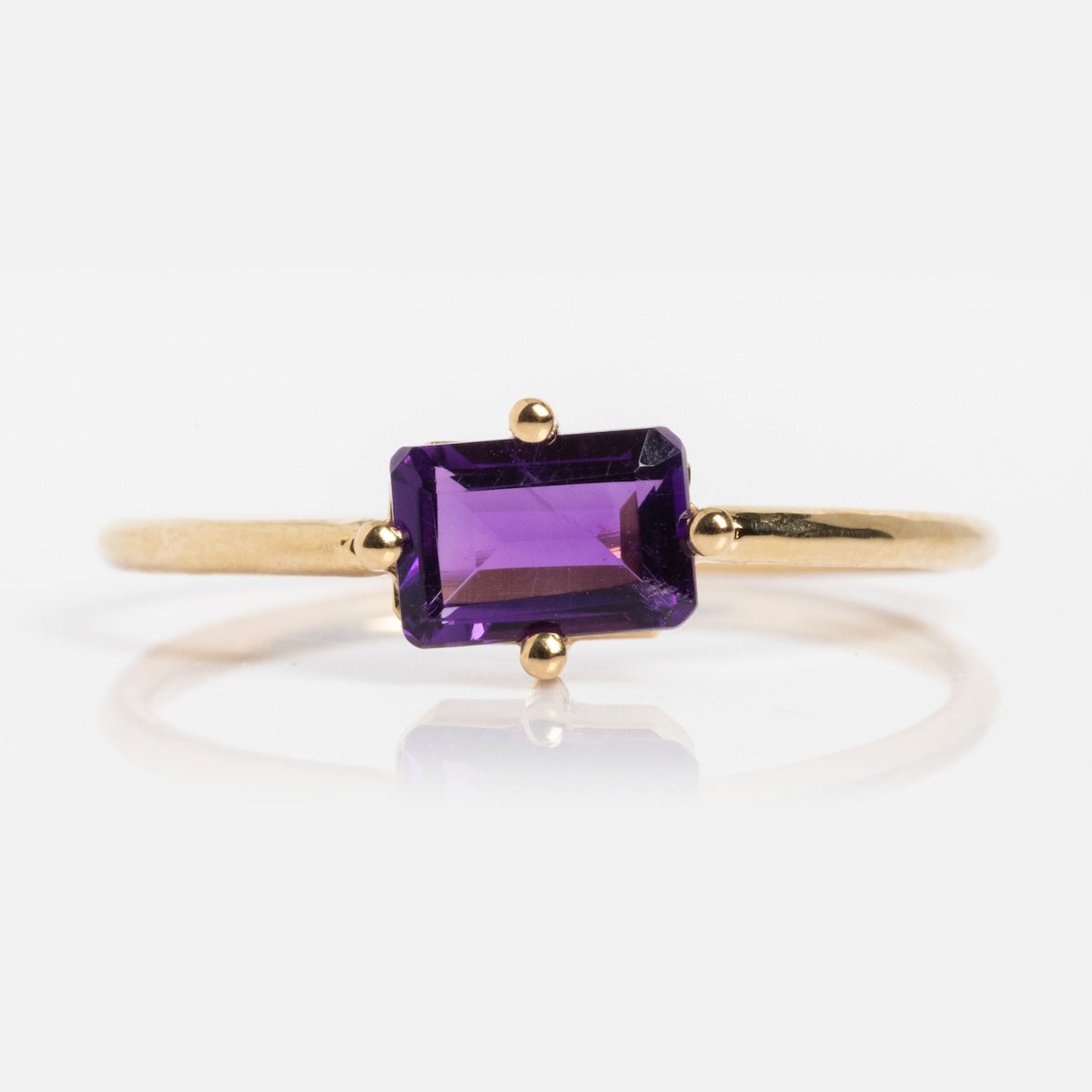The 14k Mod Love Birthstone Ring features a thin yellow gold band with a rectangular, faceted purple gemstone in a simple prong setting, displayed against a white background.