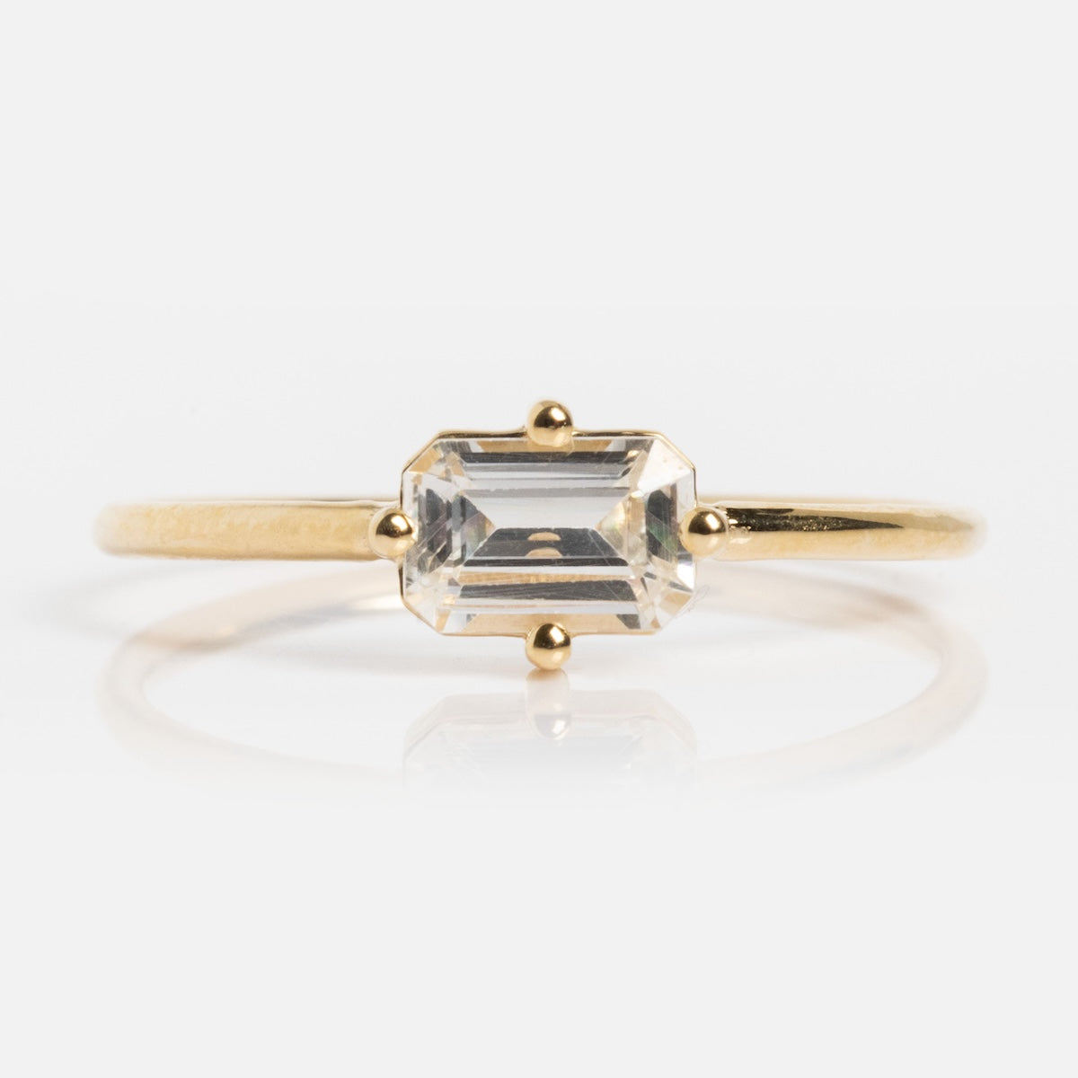 The 14k Mod Love Birthstone Ring showcases a thin yellow gold band with a rectangular emerald-cut clear gemstone in four prongs, beautifully displayed on a white background.