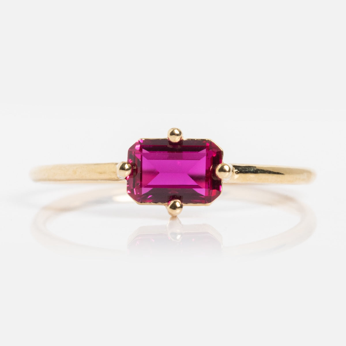 The 14k Mod Love Birthstone Ring showcases a rectangular, emerald-cut deep pink gemstone set in yellow gold with four prongs, displayed on a plain white background.