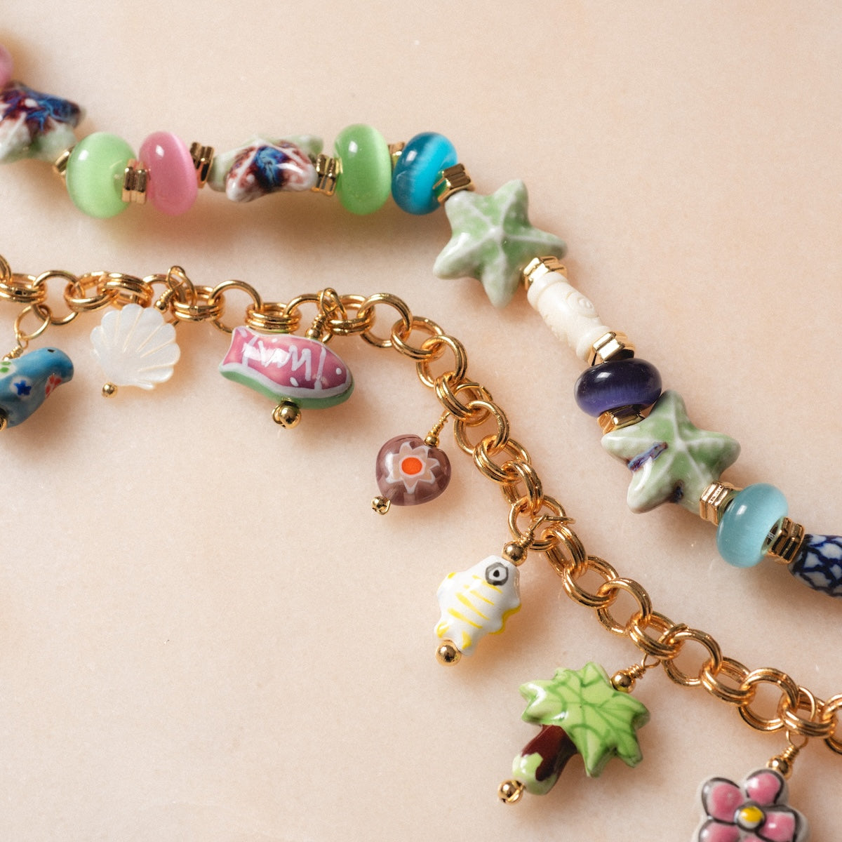 Good Idea Necklaces feature colorful beads and whimsical charms like fish, tree, shell, and star. Each playful design pops on beige marble and stands out alongside lively porcelain charm necklaces.