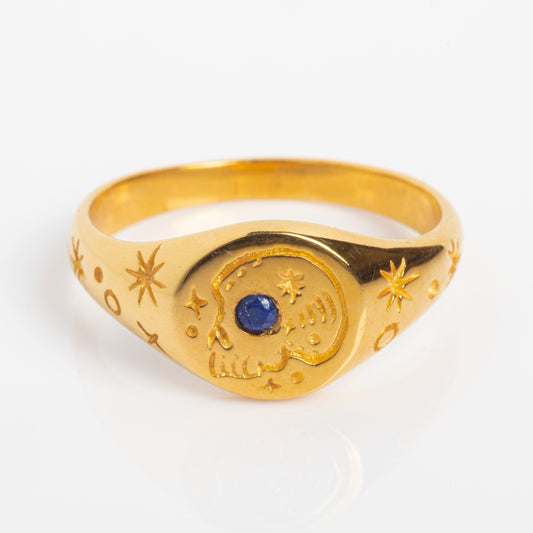 The Seer Signet Ring in 18k yellow gold vermeil features engraved stars and moons, a crescent moon on the front, and a blue sapphire at its center.