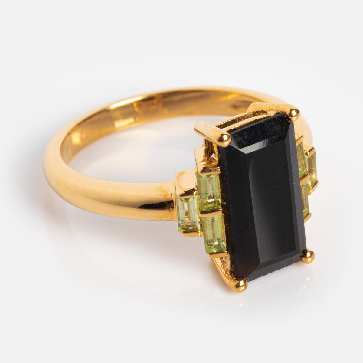 The Bold Baguette Statement Ring features 14k yellow gold plating with a large rectangular black onyx centerpiece, accented by smaller light green stones on each side for a striking look.