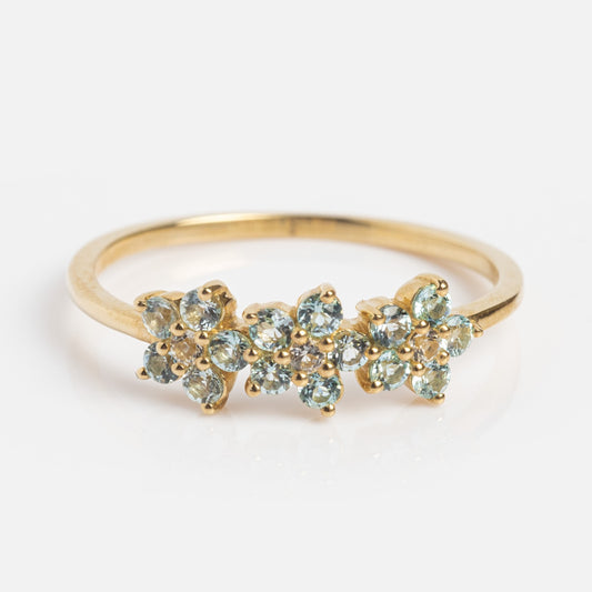 The Solid Gold Blue Topaz Flower Trio Ring showcases three clusters of small round blue topaz gemstones in a floral design, set in solid gold against a plain white background.
