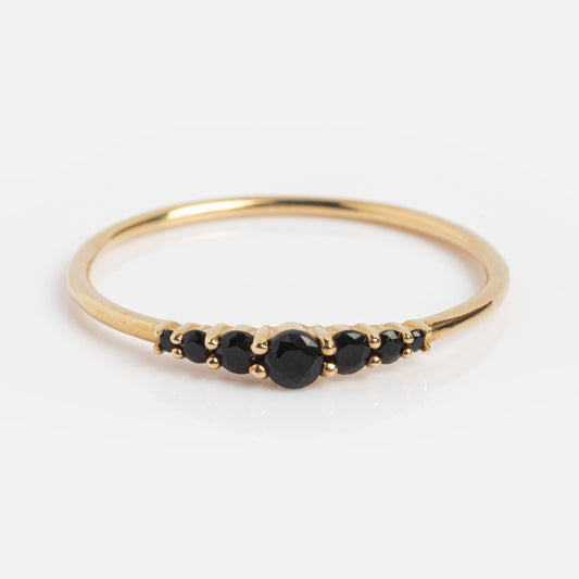 The Solid Gold Black Agate Cascade Ring is a thin stacking band with five small round black agates in a row at the center, shown against a white background.