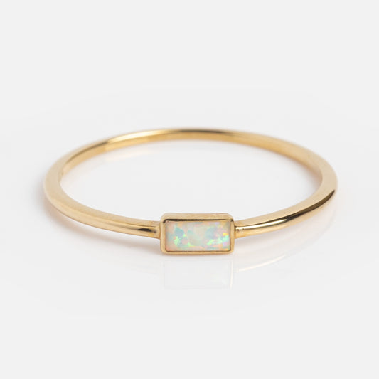 The Solid Gold Delicate Opal Ring features a rectangular iridescent opal set in solid gold, creating a minimalist Family Gold piece that shines beautifully against a white background.