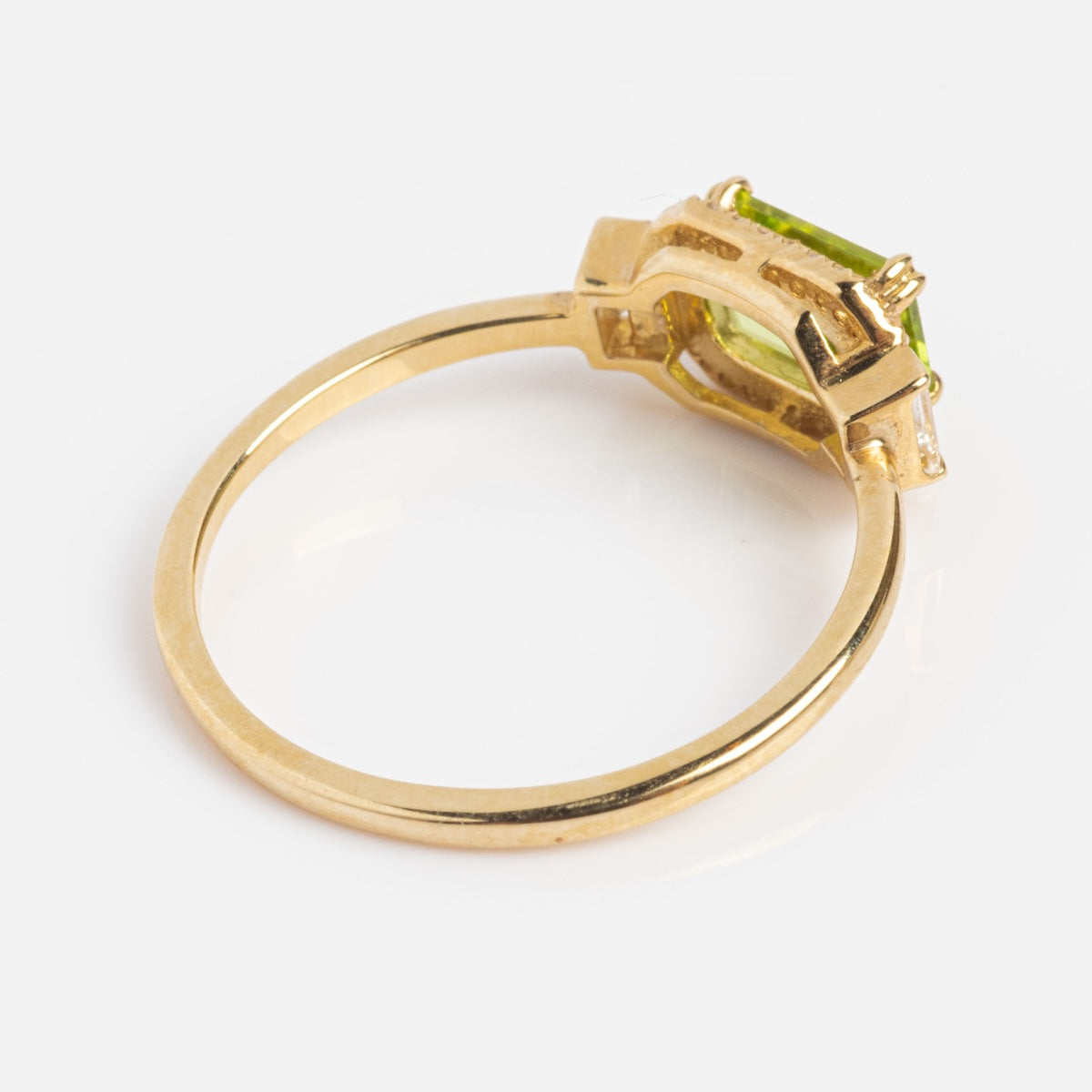 The Solid Gold Vintage Inspired East West Peridot Ring features a rectangular green peridot in a prong setting, shown at an angle to highlight the gold band and gemstone’s underside, capturing its timeless vintage charm.