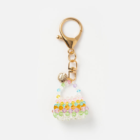 The Petite Bag Charm is a gold keychain with a lobster clasp, featuring pastel green, yellow, orange, pink, and blue beads shaped like a handbag and finished with a round gold tag—perfect for quirky bag accessory lovers.
