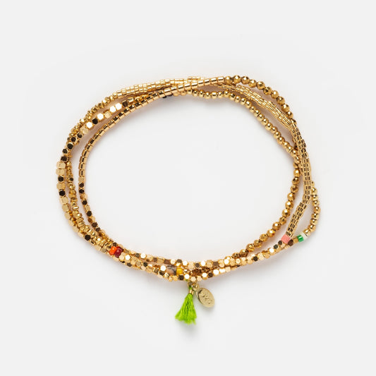 The Eliza Wrap Bracelet is a multi-strand 14k vermeil bracelet with small colored beads, a green tassel, and a round gold charm, displayed coiled on a white background.