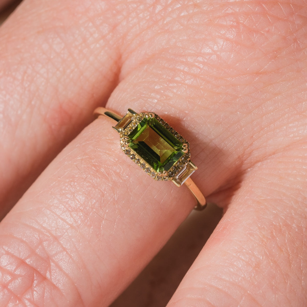 The Solid Gold Vintage Inspired East West Peridot Ring features a rectangular green gemstone with small clear accents, adding vintage charm when worn.