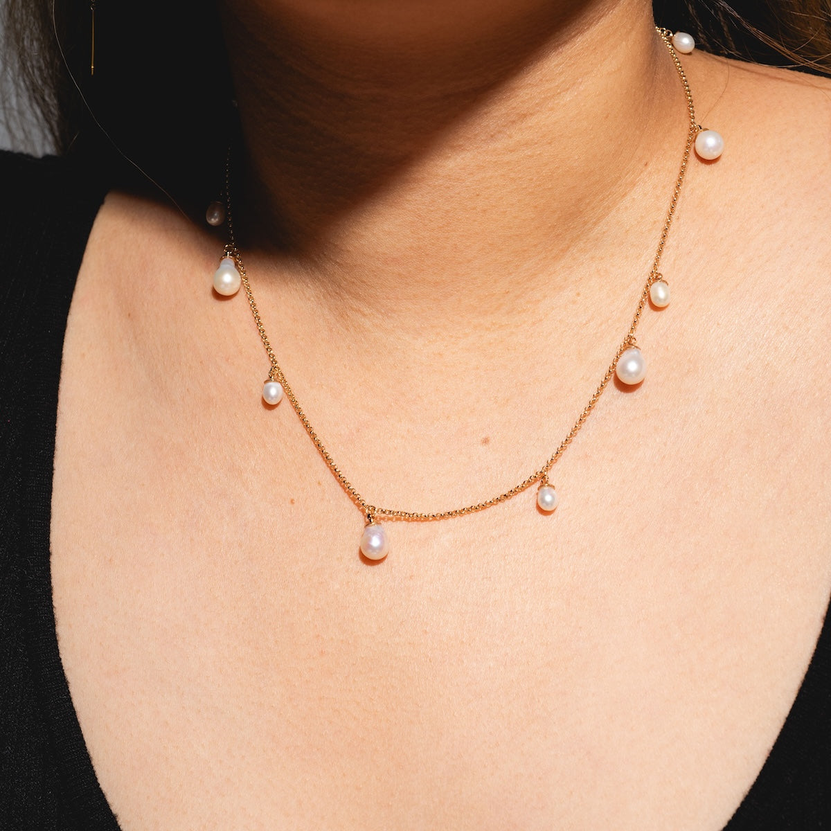 A close-up of a person wearing the Amelie Necklace Sample, a 14k yellow gold plated piece featuring small, round freshwater pearls, resting above a black top.