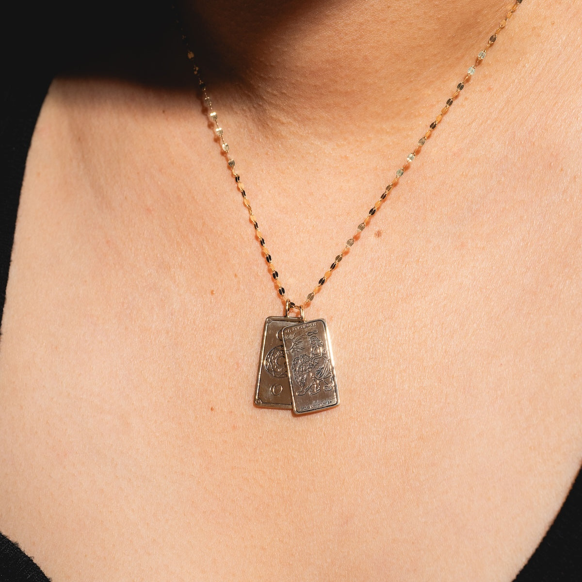 A close-up of a gold chain necklace featuring two rectangular Tarot Card Charms in 14k solid gold, resting on light skin against a black top—ideal for those who love spiritual jewelry.