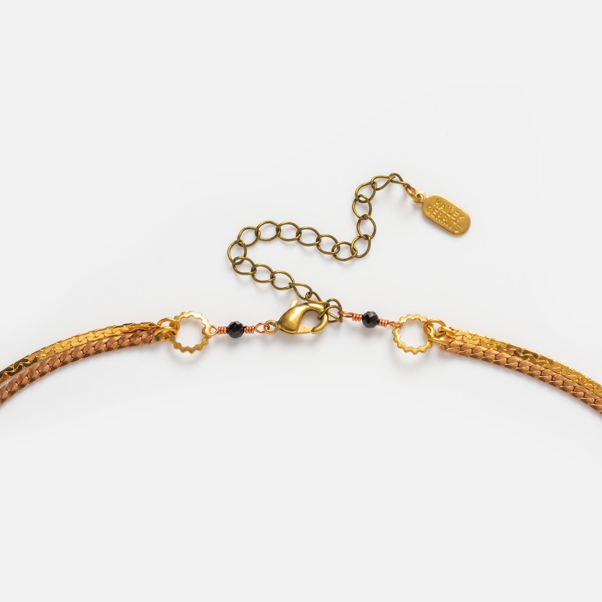 A close-up of the Palmer Gemstone Necklace, a gold layered chain with a lobster clasp, extension chain, and small decorative tag on a white background.