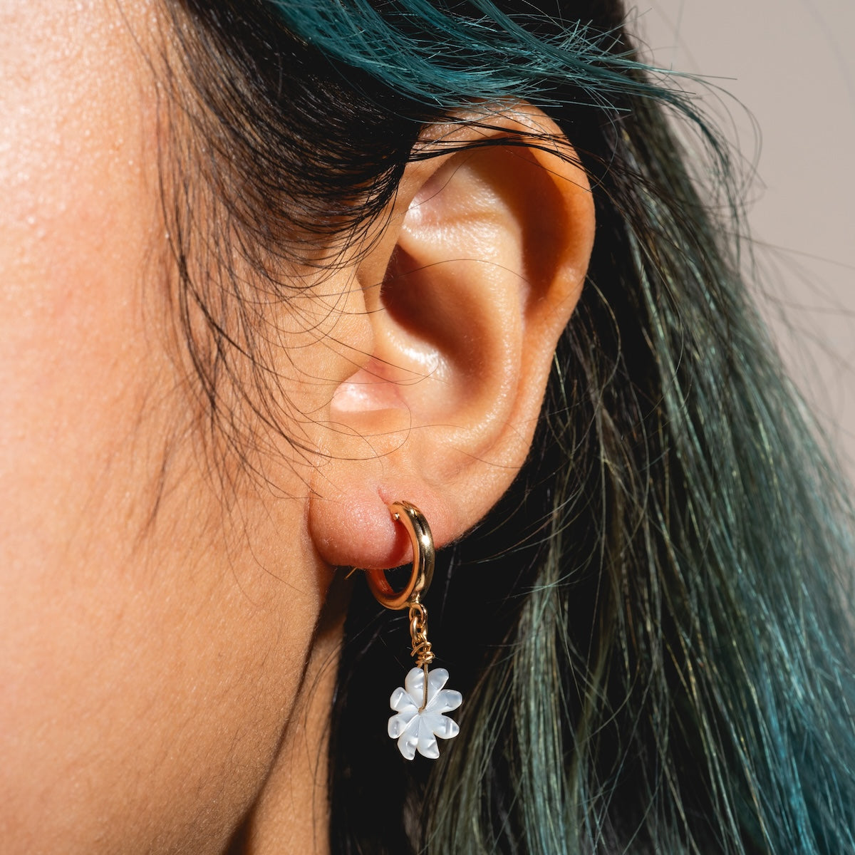 Close-up of a person with teal hair wearing the Mother of Pearl Flower Hoops Sample—handmade gold filled hoops featuring a dangling mother of pearl flower charm.