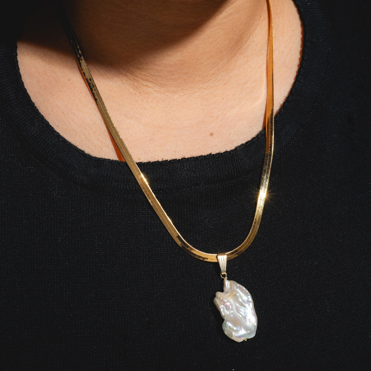 A person wearing a black top and two gold necklaces, including the Ciao Bella Necklace Sample featuring a handmade Baroque pearl pendant on a gold filled chain.